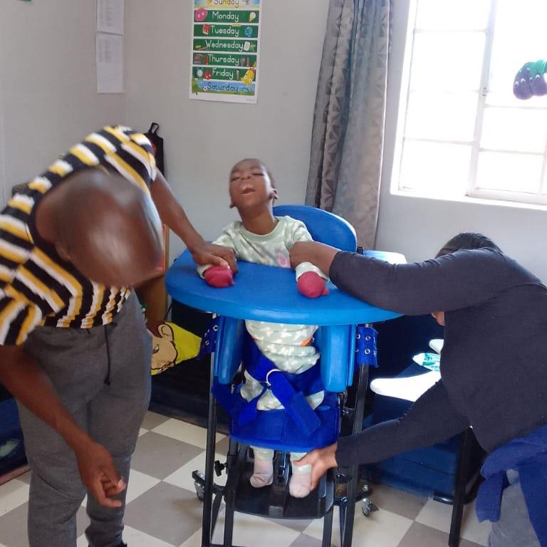 Our Physio assisting a beneficiary to stand with an assistive device